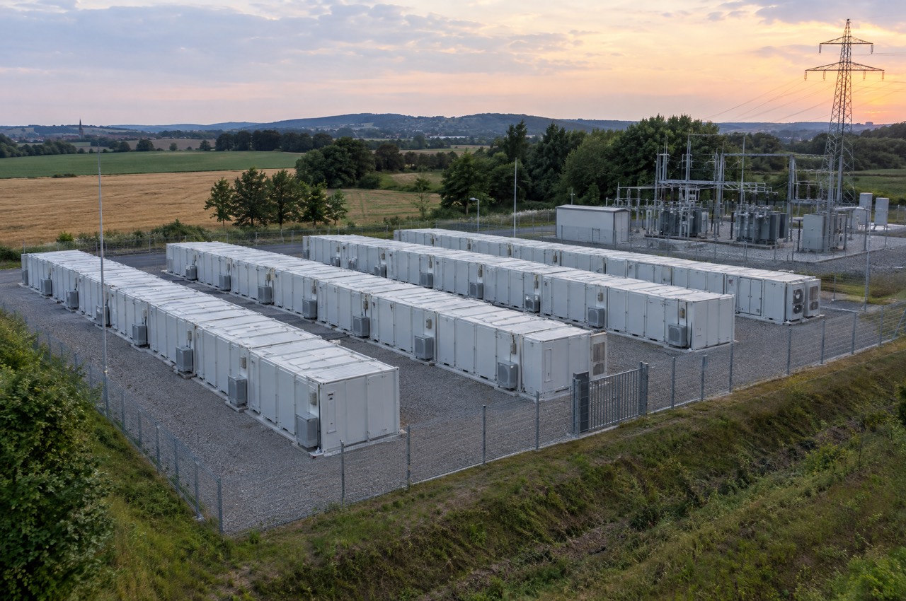 Eingezäunter Batteriespeicher-Park mit Containerreihen neben einem Umspannwerk
